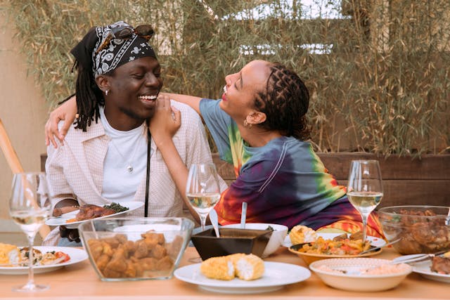 Couple laughs with large amounts of various foods on the table.